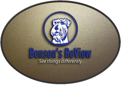 It's an oval-shaped emblem with a gold textured background. At the center, there is a circular blue outline that encloses a white stylized image of a dog's head, which appears to be a terrier breed. Directly below the circular frame, 'Benson's Review' is written in a bold serif font with 'Benson's' in blue and 'Review' in a gradient of dark to light blue, giving it a dynamic appearance. Below the name, the tagline 'See things differently' is inscribed in a smaller italicized font, suggesting a unique perspective or approach that the brand embodies. The overall design has a three-dimensional effect with a shadow, giving the impression that the logo is raised from the surface.